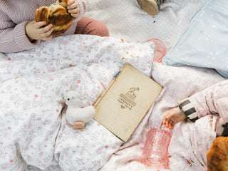 Two toddlers sitting on a Gooselings duvet with toys and a book