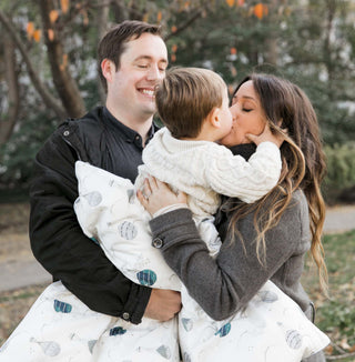 A family hugging while their toddler is wrapped in a Gooselings blanket
