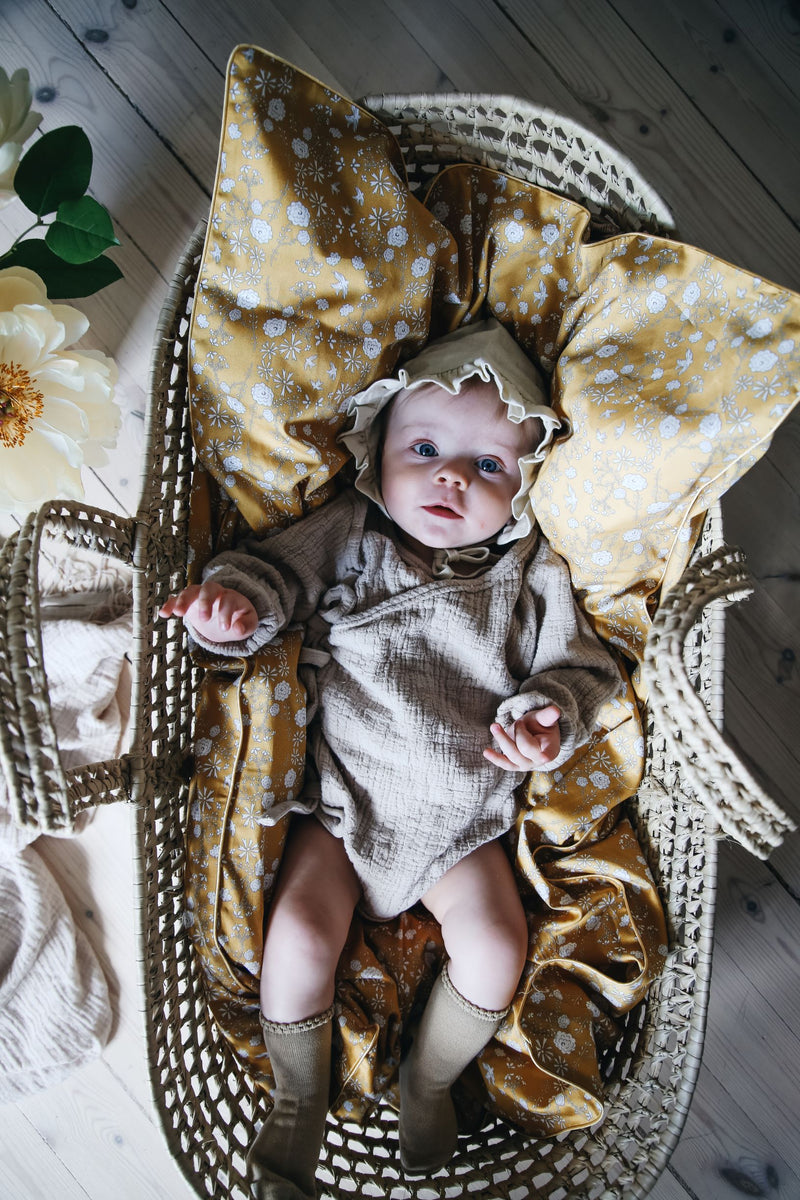 A baby resting in a woven basket while laying on top of a Gooselings pillow