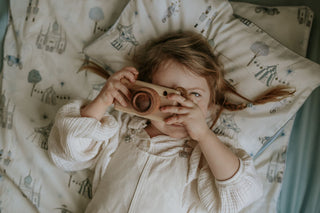 Toddler playing with wooden toy camera while resting on a Gooselings patterned pillow