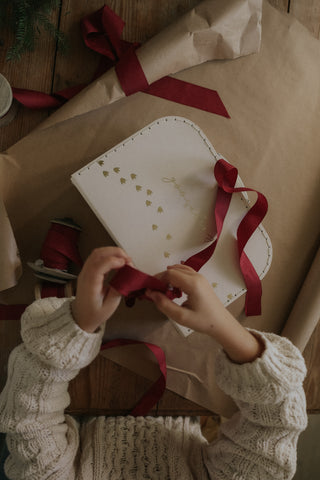 Child wrapping a gooselings box with ribbon
