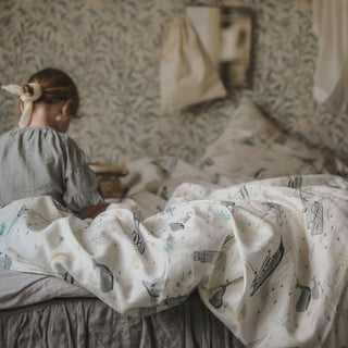 Child sitting in a twin bed reading a book with a printed duvet blanket