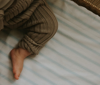 Striped blue and white crib sheet with baby sitting on top
