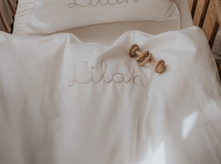 White Crib Sheet with Baby Duvet and Pillow. Wooden rattle laying on top 