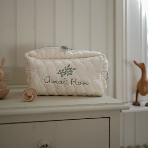 Toiletry Pouch in Ivory sitting on top pf dresser with pacifier and toys near by