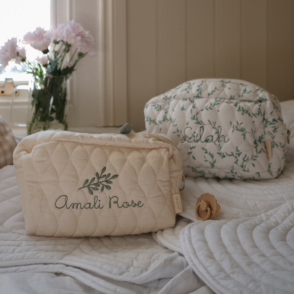 Toiletry Pouch in Ivory and Secret Garden sitting on top of bed with white flowers in the background sitting on windowsill