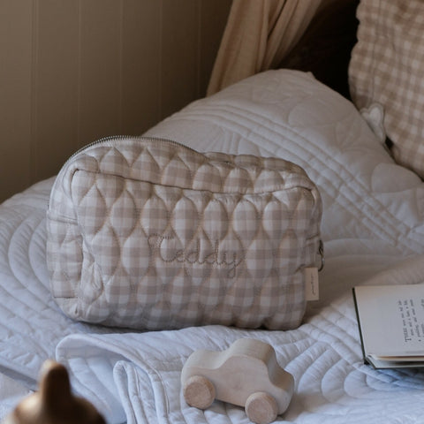 Toiletry Pouch in Beige Gingham sitting on bed with toy car and book