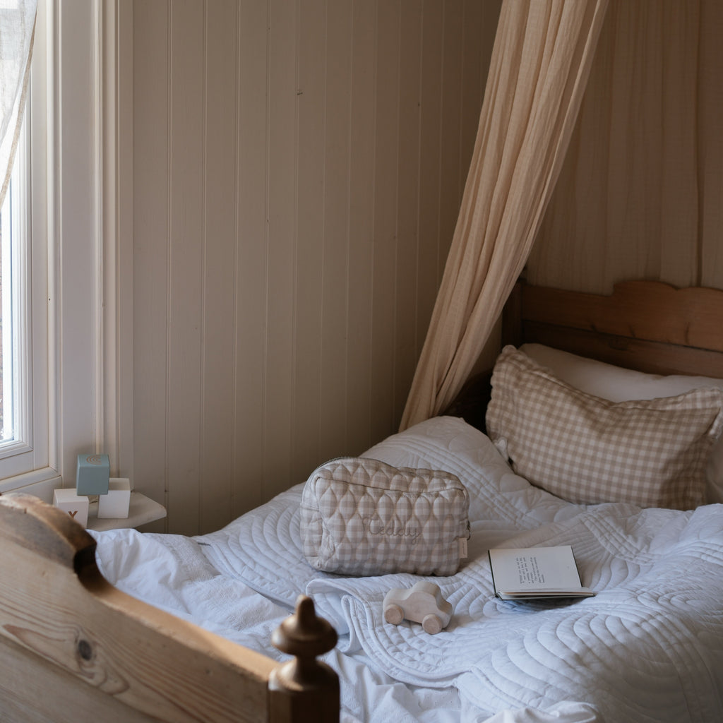 Toiletry Pouch in  Beige Gingham sitting on bed with Beige Gingham pillow. 