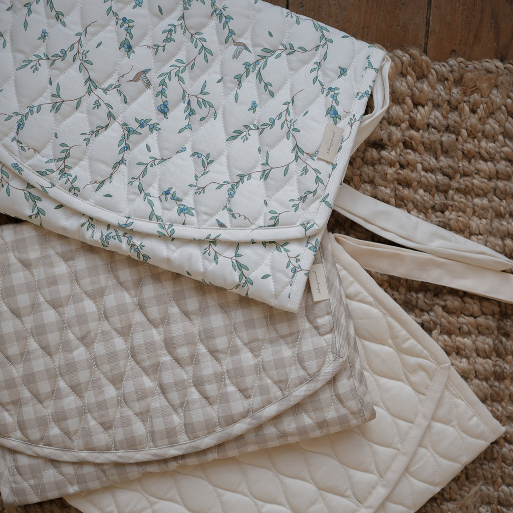 Portable Changing Pad in Beige Gingham, Secret Garden and Ivory laying flat on top of a Jute rug