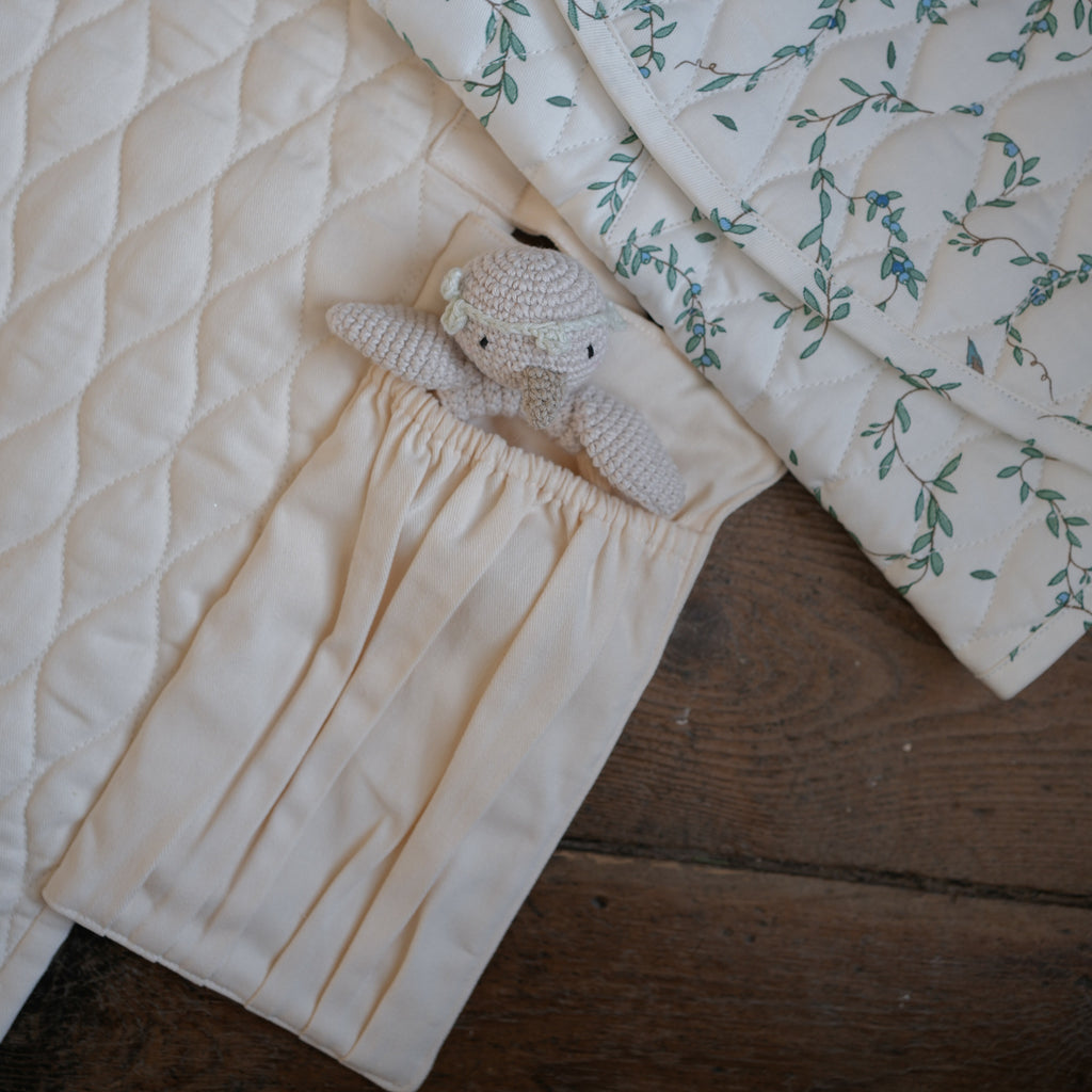 Portable Changing Pad in Ivory opened up laying flat on the floor. A folded changing pad in Secret Garden laying on top with a knit gooseling rattle in pocket