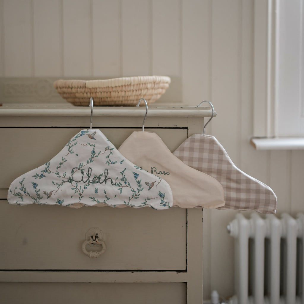 Children's Hanger in Beige Gingham, Ivory and Secret Garden hanging off top of dresser