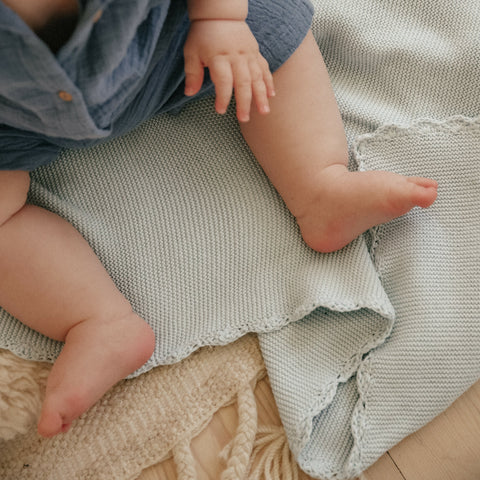 Cotton Knit Baby Blanket in Blue is laying on the floor while a baby boy is sitting and playing on top.