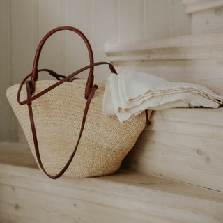 Cotton Knit Baby Blanket in Ivory next to a straw tote bag.