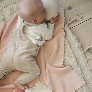 Cotton Knit Baby Blanket in Pink.  A baby is playing on her tummy with a ball while laying on top of the blanket.