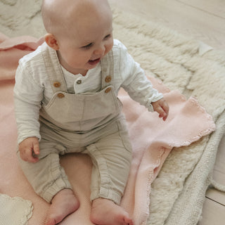 Cotton Knit Baby Blanket in Pink on the floor with a baby sitting and playing.