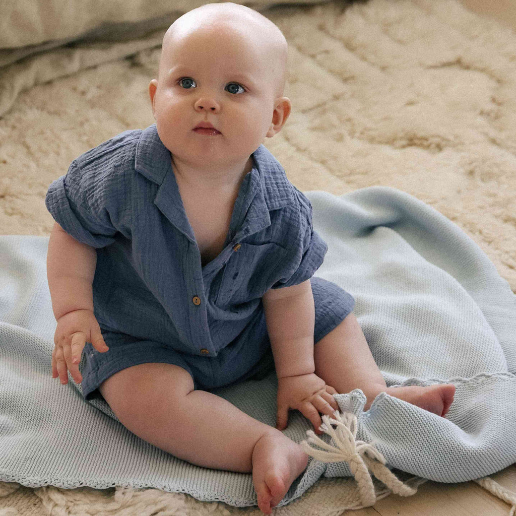 Baby sitting on ground with knit blanket in blue