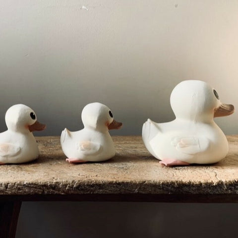 Rubber Gooseling Bath Toy in  Marshmallow. Three rubber ducks lined up in a row sitting on wooden bench.