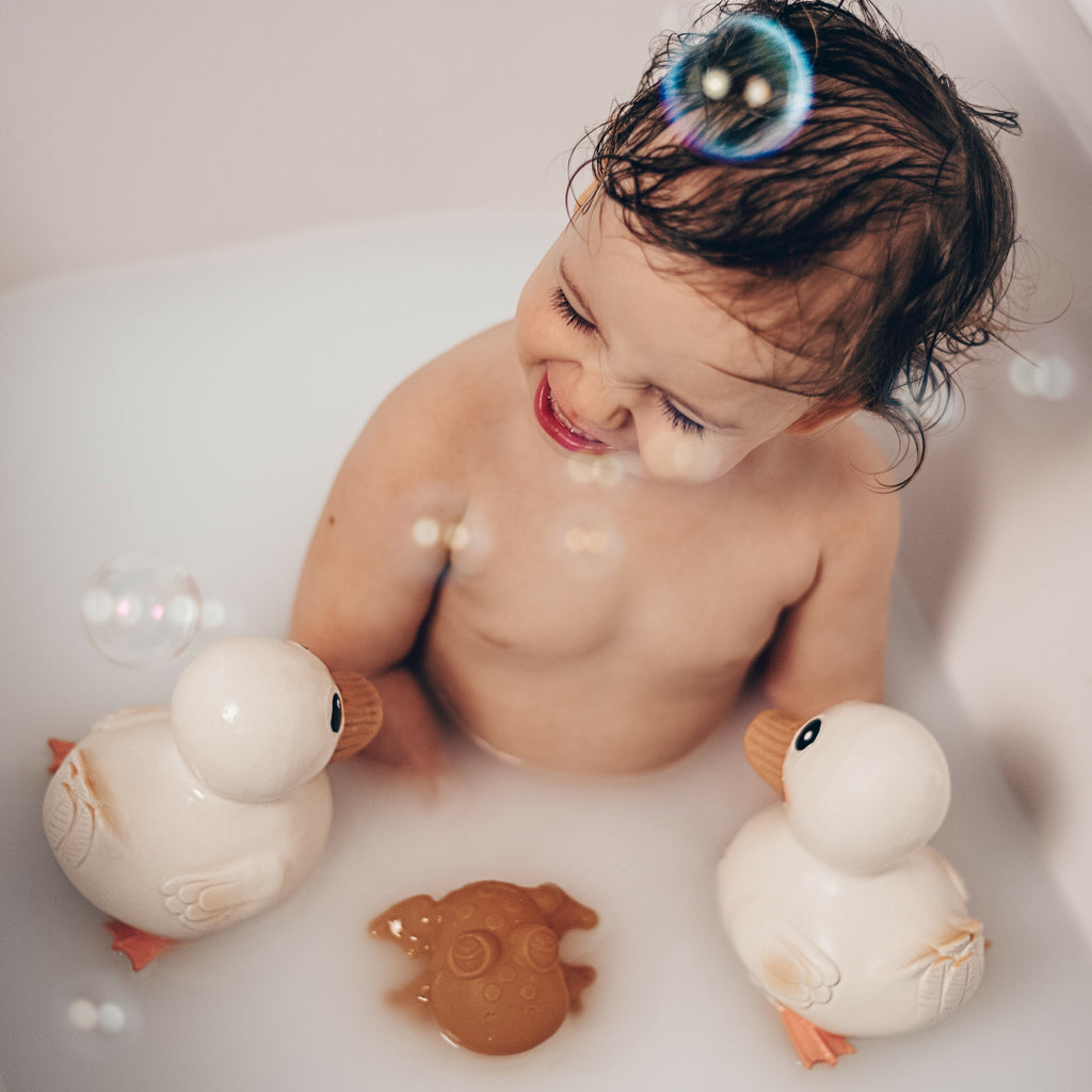 Rubber Gooseling Bath Toy in  Marshmallow. Child playing in the bubble bath with three rubber ducks