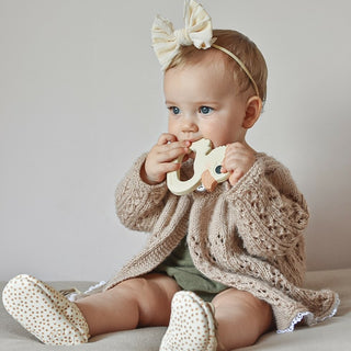 Gooseling Teether in  Marshmallow. Little girl with big bow headband uses the teether while sitting on the floor.