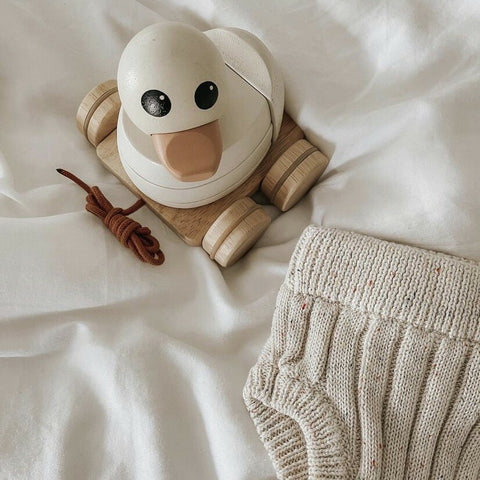 Gooseling Stacker and Pull Toy in Marshmallow. Stacker pull toy is sitting on bed with knit shorts next to it.