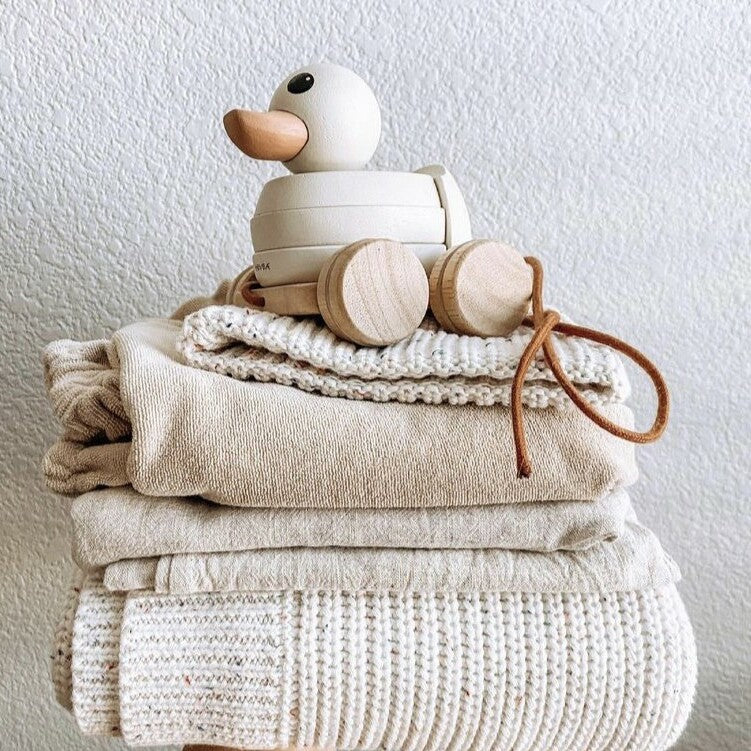 Gooseling Stacker and Pull Toy in Marshmallow sitting on top of multiple neutral colored folded knit blankets 