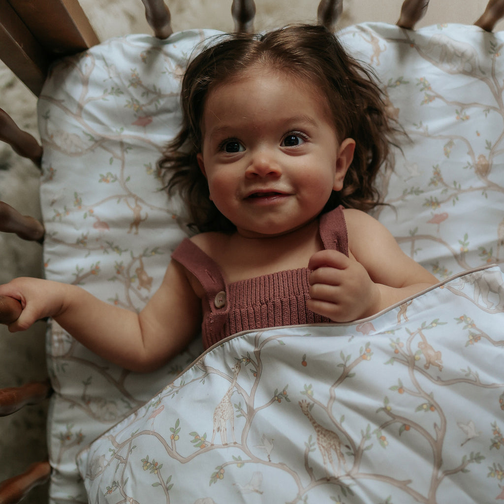 Animal Parade Crib Sheet in Blue. Child laying in crib with Duvet cover on top of her