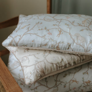 Animal Parade Toddler Pillow in Blue. Ivory and Blue printed pillows and duvet blankets folded on chair.