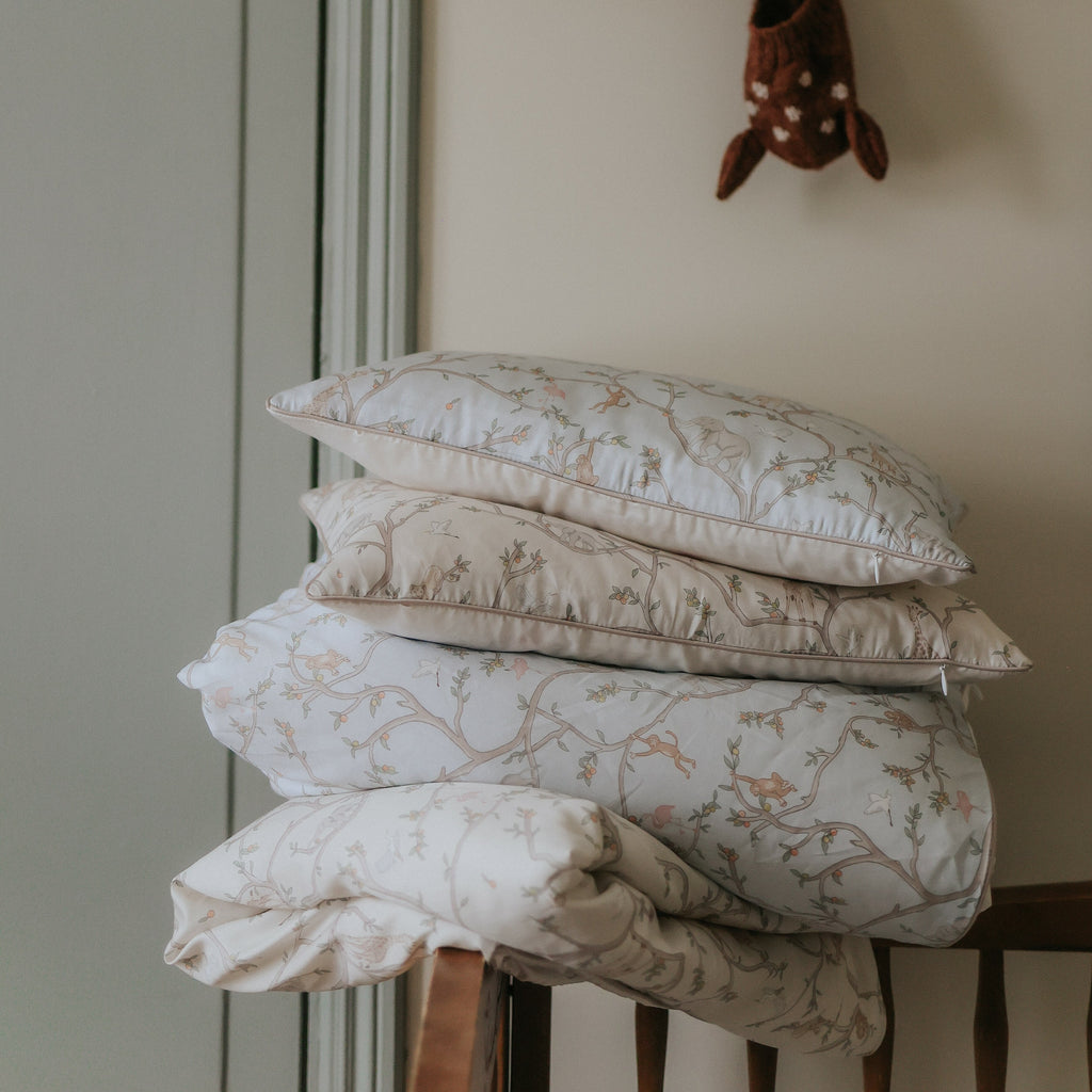 Animal Parade Baby Duvet in Blue and Ivory. Pillows and Duvets are folded and stacked on top of one another piled on top of crib