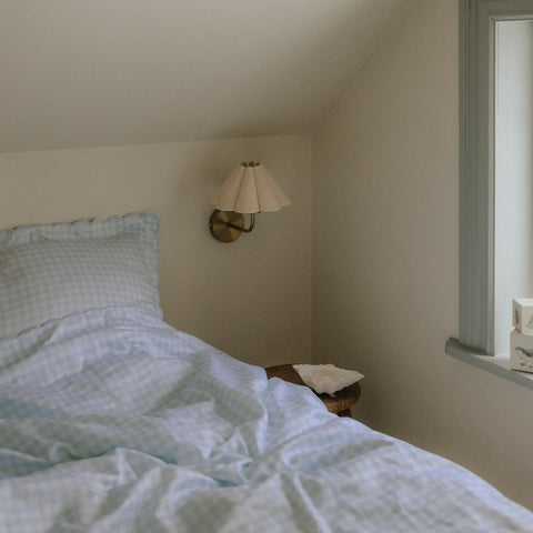 Picnic Gingham Twin Set in Blue. Both Pillow and Duvet Blanket made on bed. Next to bed is a bedside stool with decorative bowl and wall sconce above.