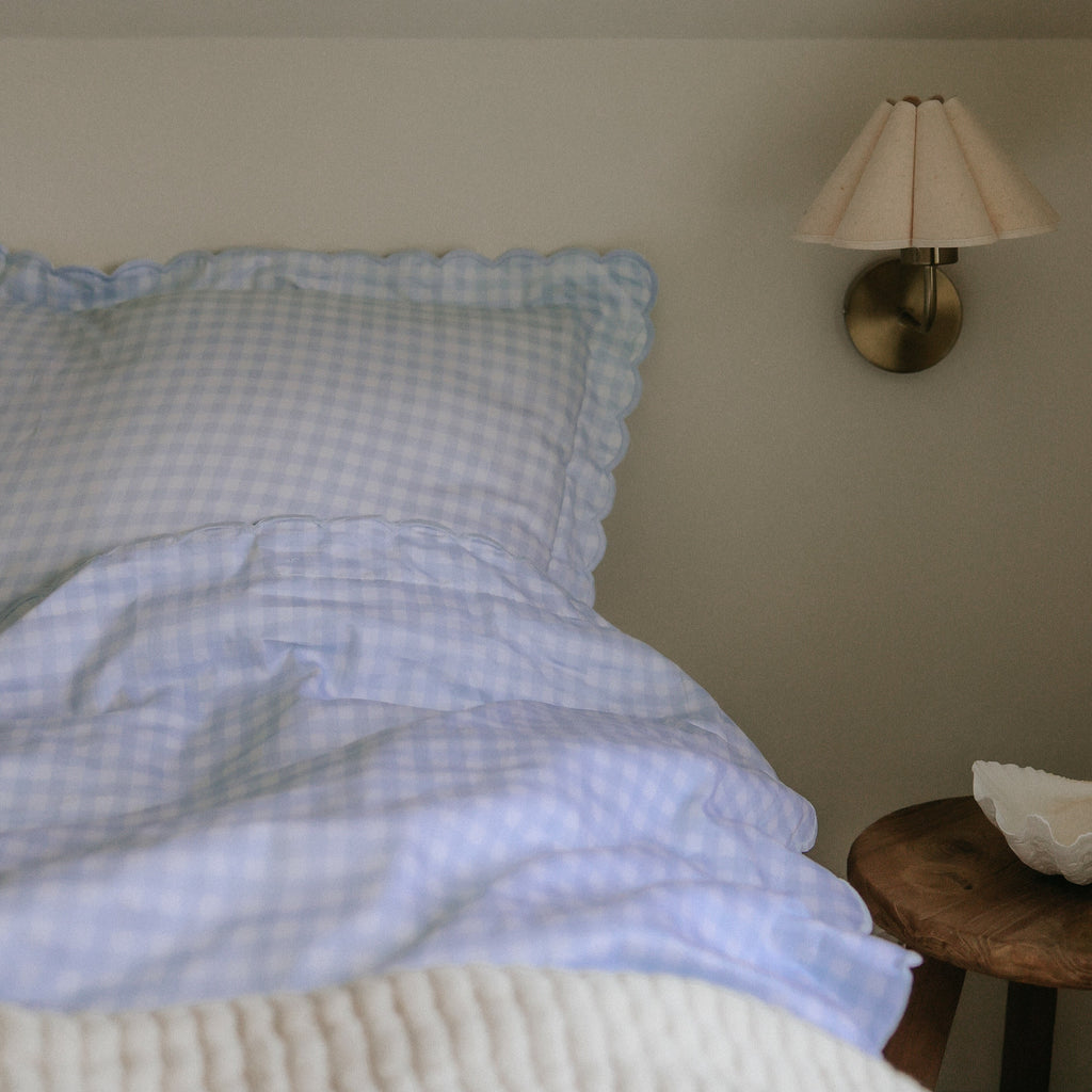 Personalize Me: Picnic Gingham Twin Set in Blue. Both Pillow and Duvet Blanket made on bed. Next to bed is a bedside stool with decorative bowl and wall sconce above.