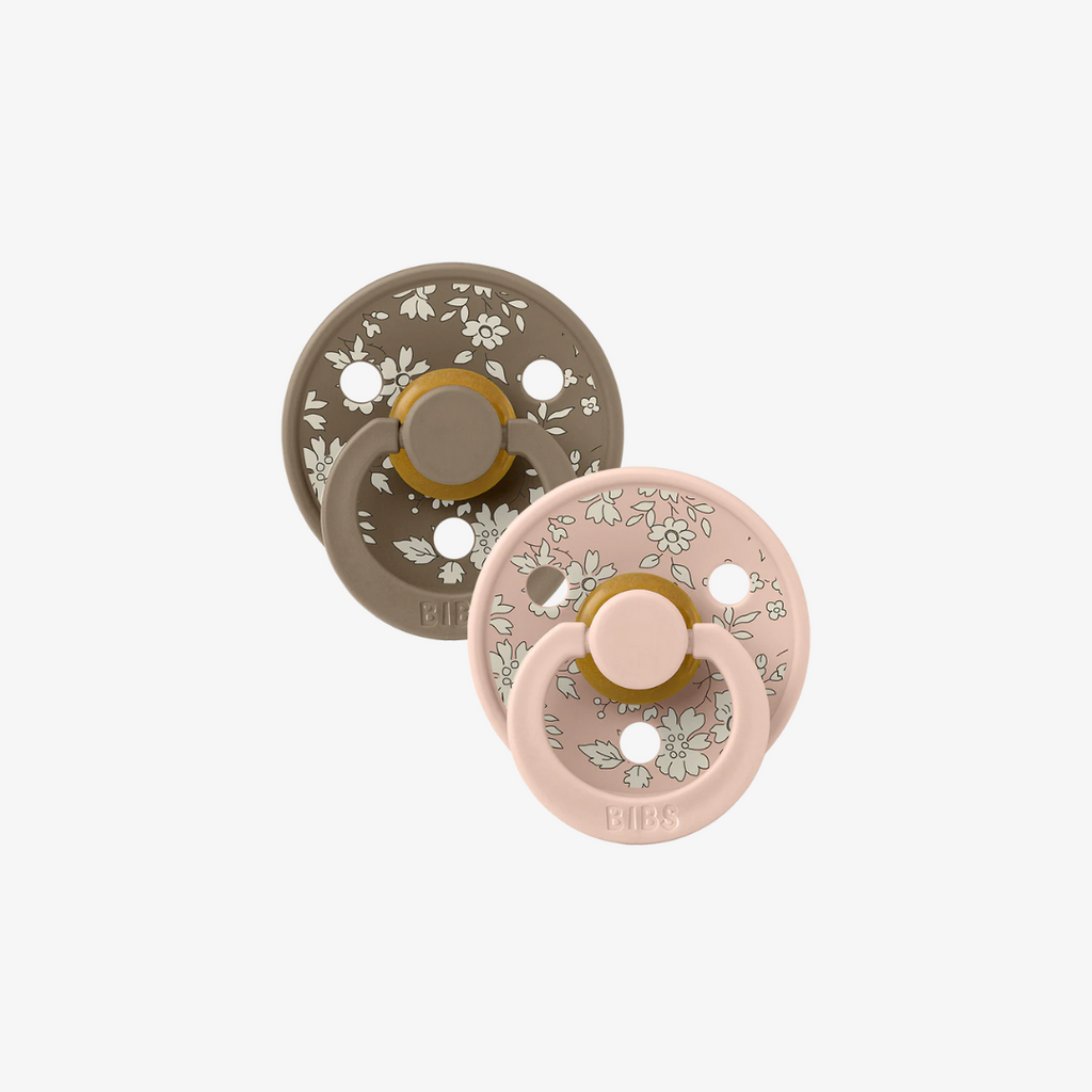 Two baby pacifiers, one brown and one pink, with floral patterns on a white background.