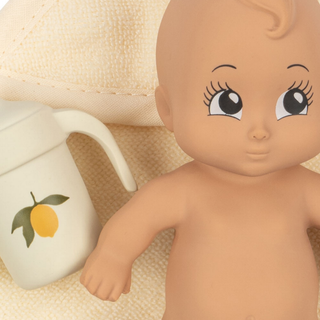 Baby doll with large eyes next to a white container with a lemon design on a beige background