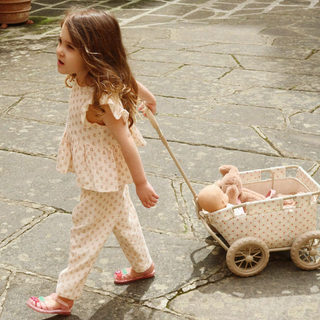 Young girl pulling a toy cart with a teddy bear on a stone pavement