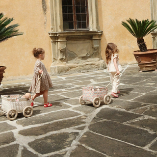Two children playing with toy wagons on a stone pavement in front of a building.