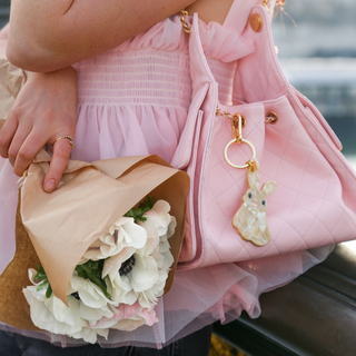 Person holding a bouquet of flowers and a pink handbag with a keychain, wearing a pink dress.
