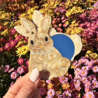 Hand holding a rabbit-shaped compact mirror against a colorful flower background