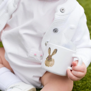 Child holding a white mug with a rabbit design outdoors