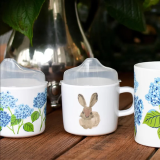 Three mugs with floral and rabbit designs on a wooden surface.