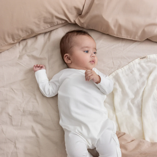 Baby in a white onesie lying on a beige bed