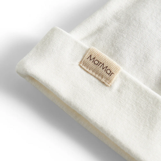 Close-up of a white baby hat with a beige tag on a light gray background