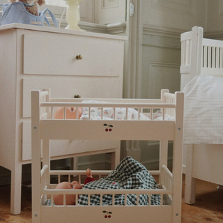 White doll crib with checkered blanket and cherry design in a nursery setting.