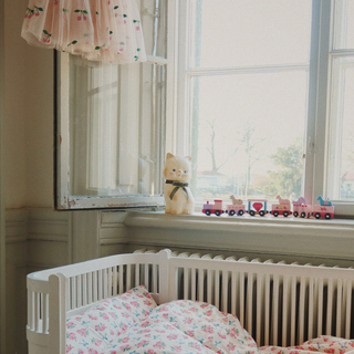 Children's room with crib, teddy bear, and toy trains by a window.