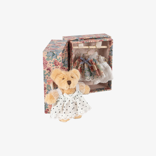 Teddy bear with a dress in front of a floral-patterned box on a white background