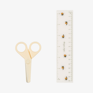 Pair of beige scissors next to a ruler on a white background