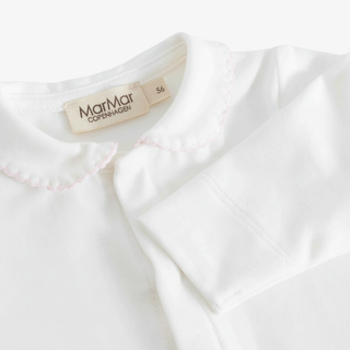 Close-up of a white long-sleeve baby top with a Peter Pan collar and light pink scalloped trim. The brand label 'MarMar Copenhagen' is visible inside the collar.