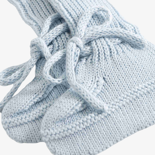 A close-up of a pair of light blue knit booties with chunky textured knit patterns and matching thick laces tied in bows.