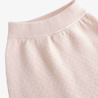 Close-up of a light pink knit garment showing the ribbed waistband and textured fabric against a plain light background.