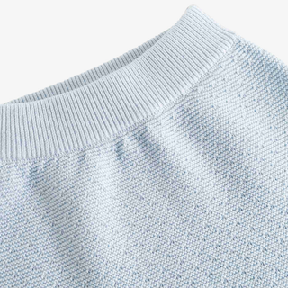Close-up of a light blue knit pants showing the ribbed waistband and fine knit texture against a plain light background.