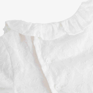 Close-up of a white textured baby top with a ruffled collar and button closure.