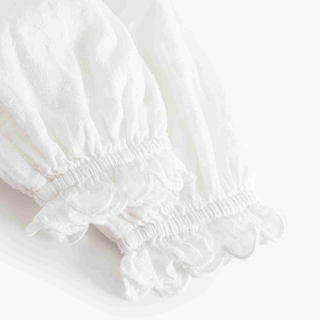 Close-up of a white textured fabric garment with gathered elastic cuffs and ruffled trim on a white background.